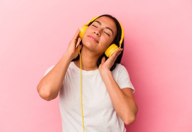 Genç Venezuelalı kadın pembe arka planda izole edilmiş müzik dinliyor.