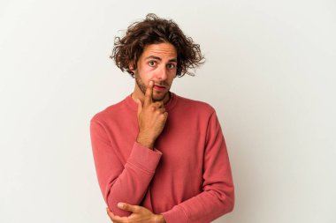 Beyaz arka planda izole edilmiş genç beyaz bir adam şüpheli ve şüpheci bir ifadeyle yana bakıyor..