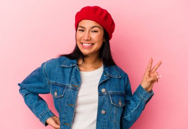 Genç Venezuelalı kadın pembe arka planda izole edilmiş zafer işareti gösteriyor ve gülümsüyor..