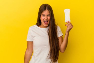 Sarı arka planda izole edilmiş kompres tutan beyaz bir kadın çok sinirli ve agresif bağırıyor..