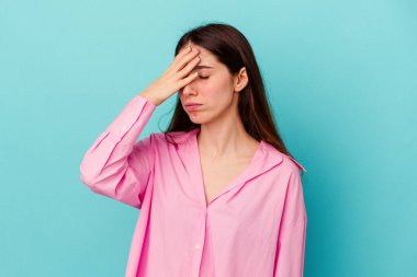 Mavi arka planda izole edilmiş genç beyaz kadın şakaklara dokunuyor ve baş ağrısı çekiyor..