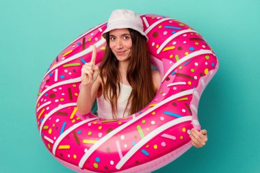 Mavi arka planda izole edilmiş şişme donutu olan beyaz bir kadın, parmak izleriyle bir numarayı gösteriyor..