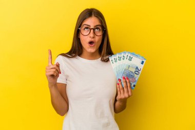 Sarı arka planda izole edilmiş banknotlar tutan beyaz bir kadın ağzı açık bir şekilde üst tarafı işaret ediyor..