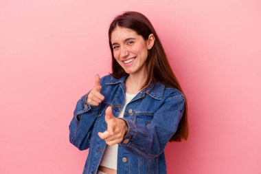 Pembe arka planda izole edilmiş genç beyaz kadın parmaklarıyla ön tarafı işaret ediyor..