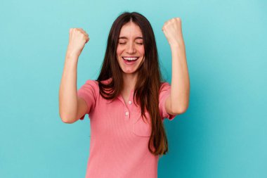 Genç beyaz kadın mavi arka planda izole edilmiş tasasız ve heyecanlı bir şekilde tezahürat yapıyor. Zafer konsepti.