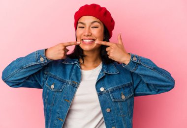 Venezuelalı genç bir kadın pembe arka planda izole edilmiş gülümsüyor, parmaklarını ağzına doğrultuyor..