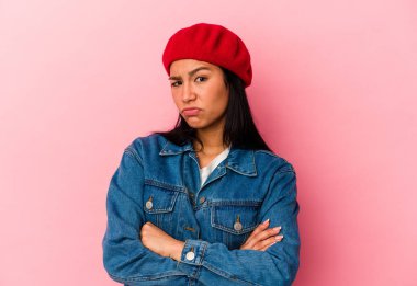 Venezuelalı genç bir kadın pembe arka planda izole edilmiş hoşnutsuzca kaşlarını çatmış, kollarını kavuşturmuş..