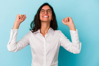 Mavi arka planda izole edilmiş genç beyaz kadın zaferi, tutkuyu ve coşkuyu kutluyor, mutlu bir ifade..