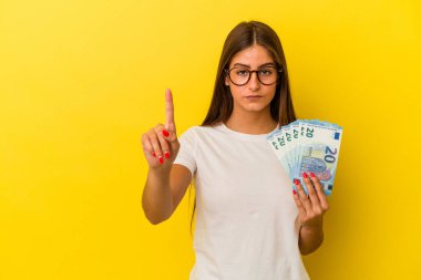 Sarı arka planda izole edilmiş banknotları tutan beyaz bir kadın bir numarayı parmağıyla gösteriyor..