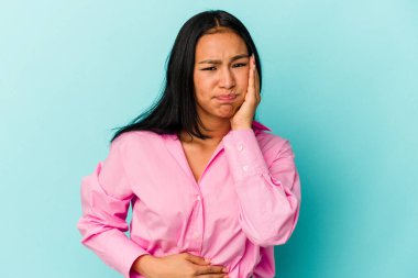 Mavi arka planda izole edilmiş genç Venezuelalı kadın yanakları patlatıyor, yorgun bir ifade takınıyor. Yüz ifadesi kavramı.