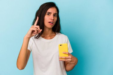 Elinde cep telefonu olan beyaz bir kadın mavi arka planda izole bir şekilde duruyor. Bir fikri, ilham verici bir fikri var..