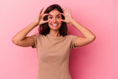 Pembe arka planda izole edilmiş genç beyaz kadın bir başarı fırsatı bulmak için gözlerini açık tutuyor..