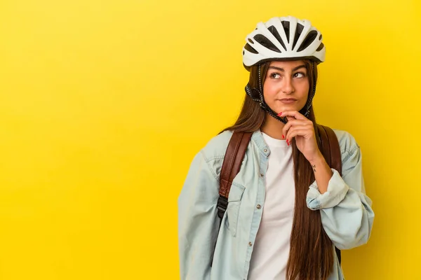 若いです学生Caucasian女性身に着けていますAバイクヘルメット隔離された黄色の背景見ます横に疑いと懐疑的な表情 — ストック写真