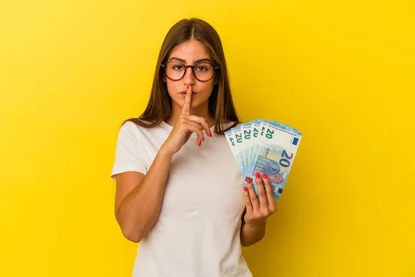 Young Caucasian Woman Holding Bills Isolated Yellow Background Keeping Secret — Stock Photo, Image
