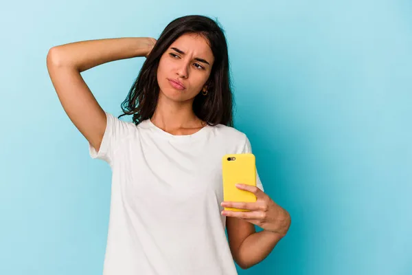 年轻的高加索女人拿着一部蓝色背景的手机 背对着头 思考着 做出选择 — 图库照片