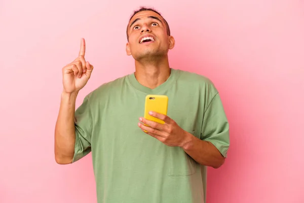 Młody Wenezuelczyk Trzyma Telefon Komórkowy Odizolowany Różowym Tle Wskazując Góry — Zdjęcie stockowe