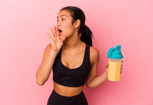 若いベネズエラの女性はピンクの背景叫びに隔離されたタンパク質シェイクを飲むと口を開けた近くに手のひらを保持 — ストック写真