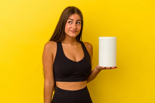 黄色の背景に単離されたタンパク質ボトルを持っている若い白人女性は目標と目的を達成することを夢見て — ストック写真