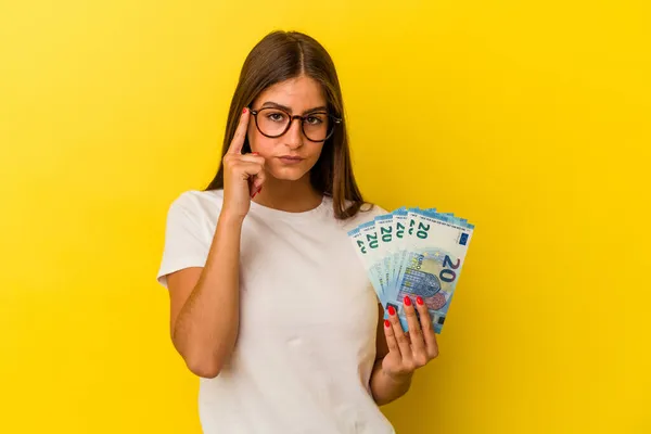 Young Caucasian Woman Holding Bills Isolated Yellow Background Pointing Temple — Stock Photo, Image