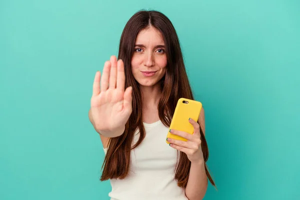 Mladá Běloška Drží Mobilní Telefon Izolovaný Modrém Pozadí Stojí Nataženou — Stock fotografie