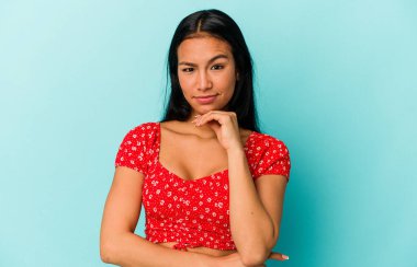 Genç Venezuelalı bir kadın mavi arka planda izole edilmiş şüpheli, belirsiz, seni muayene ediyor..