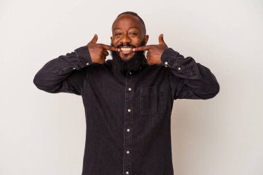 Sakallı Afro-Amerikan bir adam pembe arka planda izole edilmiş gülümsüyor, parmaklarını ağıza doğrultuyor..