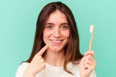 Mavi arka planda diş fırçası tutan beyaz bir kadın.