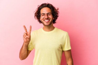 Kafkasyalı genç adam pembe fırında izole edilmiş neşeli ve kaygısız parmaklarıyla barış sembolü gösteriyor..