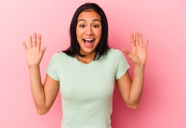 Genç Venezuelalı bir kadın pembe arka planda izole edilmiş. Hoş bir sürprizle karşılaşıyor, heyecanlı ve el kaldırıyor..