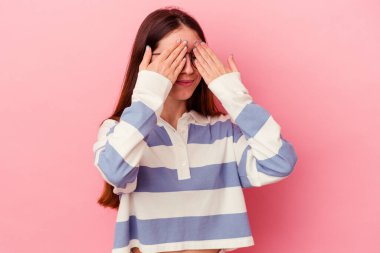 Pembe arka planda izole edilmiş genç beyaz kadın elleriyle gözlerini kapatmaktan korkuyor..