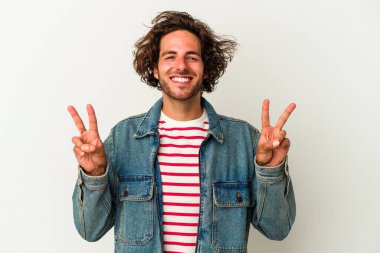 Beyaz arka planda izole edilmiş genç beyaz bir adam zafer işareti gösteriyor ve gülümsüyor..