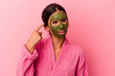 Pembe arka planda izole edilmiş bornoz ve yüz maskesi takan beyaz bir kadın işaret parmağıyla hayal kırıklığı jesti yaptığını gösteriyor..