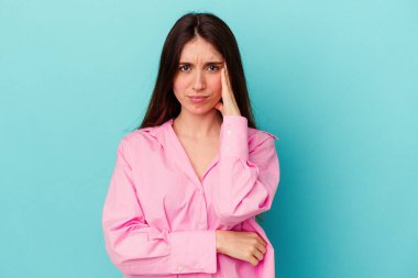 Mavi arka planda izole edilmiş genç beyaz kadın yanakları patlatıyor, yorgun bir ifadesi var. Yüz ifadesi kavramı.