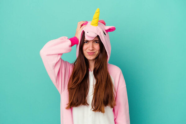 Young caucasian woman wearing a unicorn pajama isolated on blue background being shocked, she has remembered important meeting.