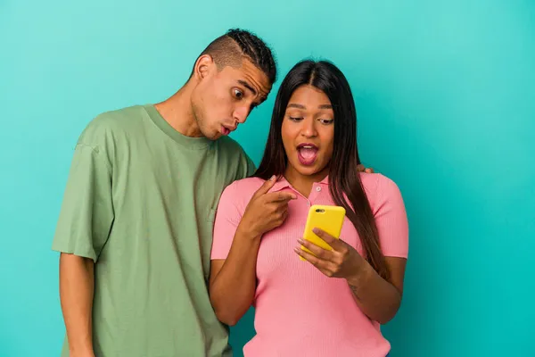 Young latin couple with a mobile phone isolated on blue background