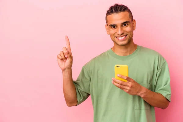 Młody Wenezuelczyk Telefonem Komórkowym Różowym Tle Pokazuje Numer Jeden Palcem — Zdjęcie stockowe