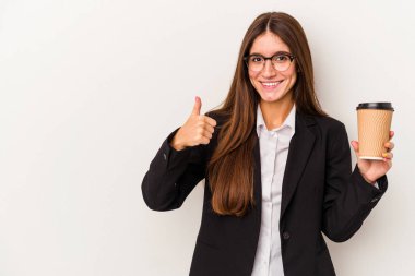 Beyaz arka planda izole edilmiş kahve içen beyaz iş kadını gülümsüyor ve başparmağını kaldırıyor.