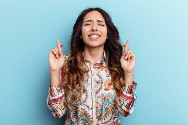 Mavi arka planda izole edilmiş genç Meksikalı kadın şans dilemek için şans diliyor.