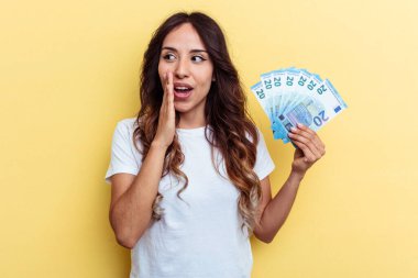 Sarı arka planda izole edilmiş banknotları tutan genç melez kadın gizli bir fren haberinin olduğunu ve kenara baktığını söylüyor.