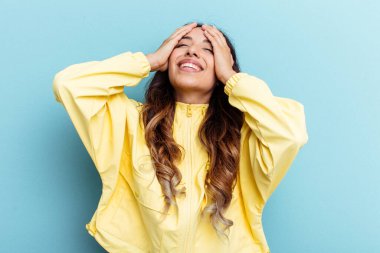 Mavi arka planda izole edilmiş genç Meksikalı kadın mutlu bir şekilde ellerini başının üstünde tutuyor. Mutluluk kavramı.