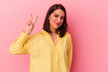 Genç beyaz kadın pembe arka planda izole edilmiş neşeli ve kaygısız parmakları olan bir barış sembolü gösteriyor..