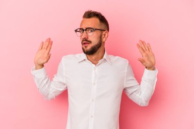 Pembe arka planda izole edilmiş dövmeleri olan beyaz genç bir adam yakın bir tehlike nedeniyle şoka uğruyor.