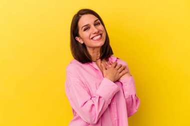 Sarı arka planda izole edilmiş genç beyaz kadın, dost canlısı bir ifadeye sahip, avuçlarını göğsüne bastırıyor. Aşk konsepti.