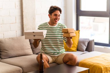 Genç melez adam pizza yiyor, burger yiyor ve bira içiyor.