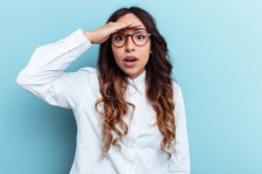 Mavi arka planda izole edilmiş genç Meksikalı kadın uzaklara bakıyor ve elini alnına koyuyor..