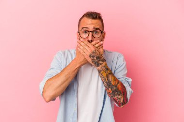 Pembe arka planda dövmeleri olan beyaz bir genç adam elleri ile ağzını kapatırken şoka uğramış..