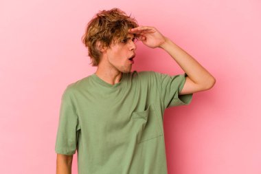 Makyajlı beyaz bir adam pembe arka planda soyutlanmış, uzaklara bakıyor ve elini alnına koyuyor..