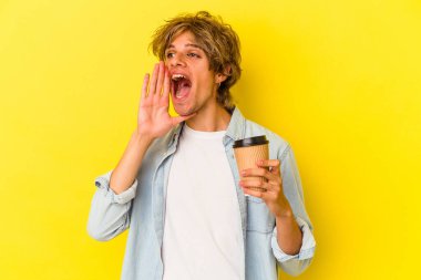 Elinde makyaj malzemesi olan beyaz bir adam sarı arka planda izole edilmiş kahve tutuyor bağırıyor ve avuç içini açık tutuyor..