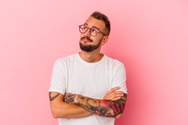 Pembe arka planda, hedeflerine ve amaçlarına ulaşma hayali kuran, dövmeleri olan beyaz bir genç.