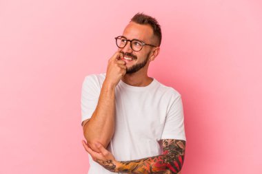 Pembe arka planda izole edilmiş beyaz dövmeli genç bir adam rahatlamış fotokopi odasına bakan bir şey düşünüyor..